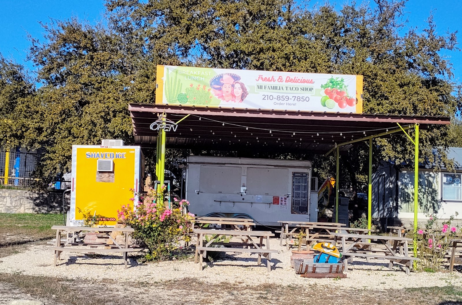 Mi Familia Taco Shop food truck with breakfast and lunch menu sign, tucked under a shaded patio with string lights and picnic tables