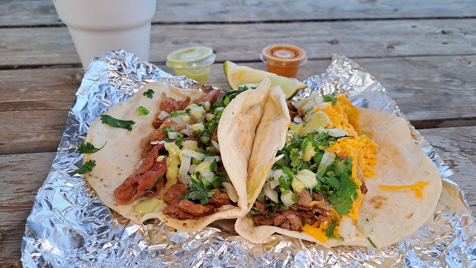 Breakfast tacos with fresh cilantro, onion, and cheese wrapped in foil, served with lime and salsa