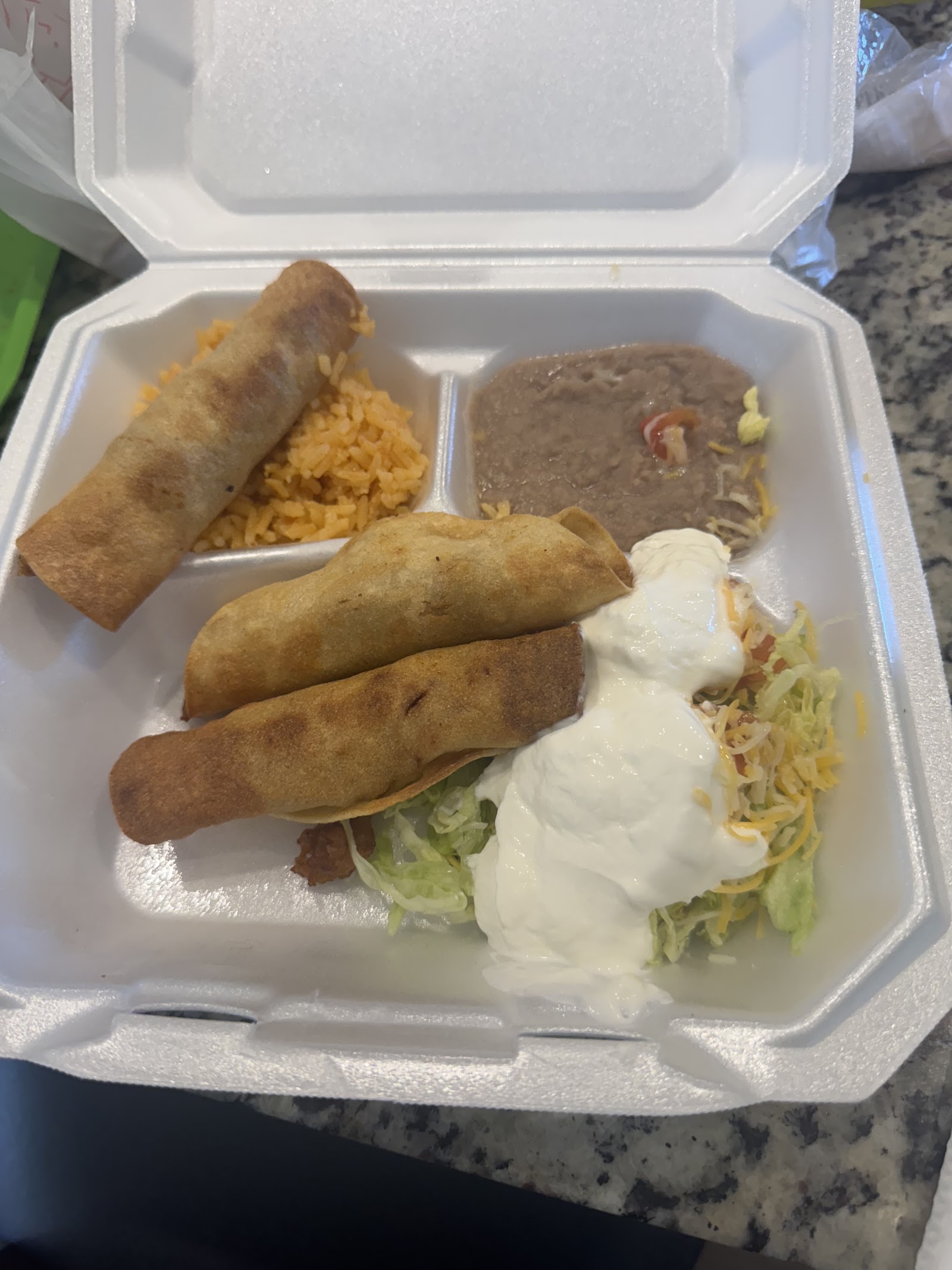 To-go plate with taquitos, Mexican rice, refried beans, and a fully loaded taco with sour cream