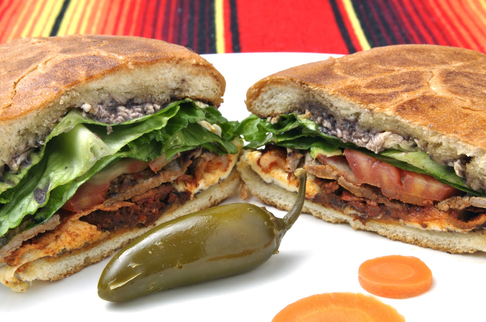 Torta sandwich sliced in half, loaded with meat, lettuce, and tomato